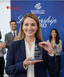 Woman holding a clear award with 'Golden City Decor Works' and 'Leadership Award' text, standing in front of a blue backdrop with people clapping.