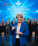 Woman holding an award with a backdrop of people clapping at a Humanitarian Award Gala event.