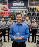Man holding an award in a car parts store with colleagues clapping