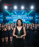 Woman holding an award on a stage with 'Odyssey Relocation' and 'Senior Consultant of the Year Awards' text.