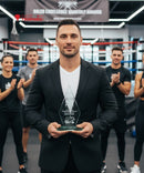 Man holding an award in a boxing ring with people clapping in the background