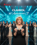 Woman holding an award with a Clairol 30th Anniversary Gala backdrop featuring other attendees.
