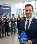 Man in a suit holding a Subaru award in a car dealership setting