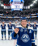 Hockey player holding a trophy with teammates in the background on an ice rink.